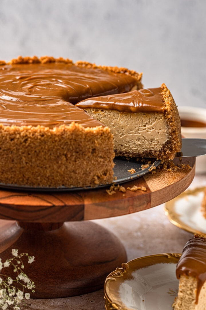 Dulce de leche cheesecake on a cake stand. One slice is being taken.