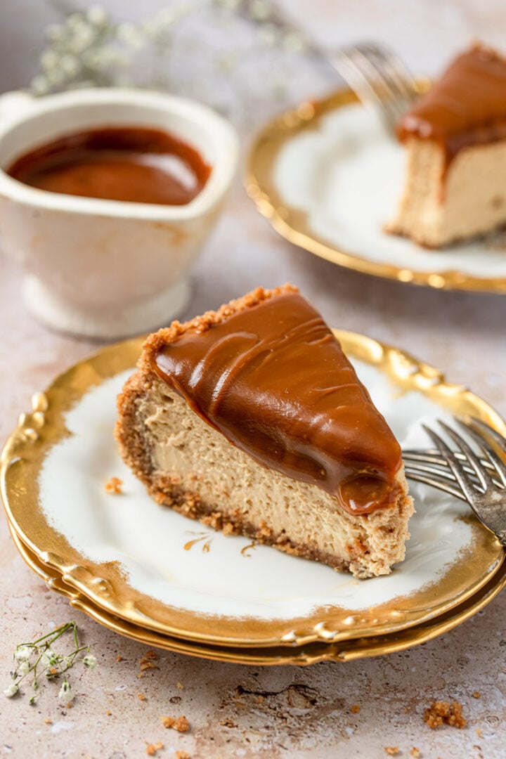 A slice of dulce de leche cheesecake topped with dulce de leche sauce on two stacked dessert plates.
