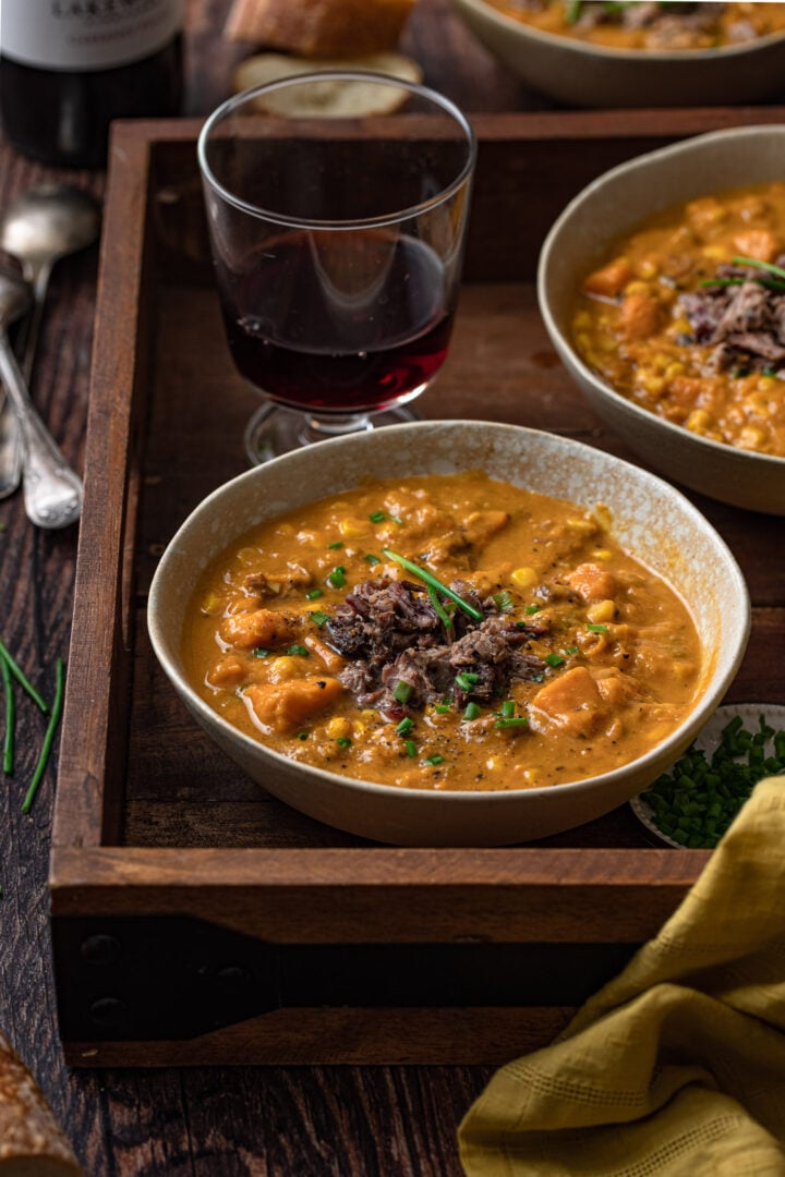 Two bowls of sweet potato chowder on a tray with a glass of wine.