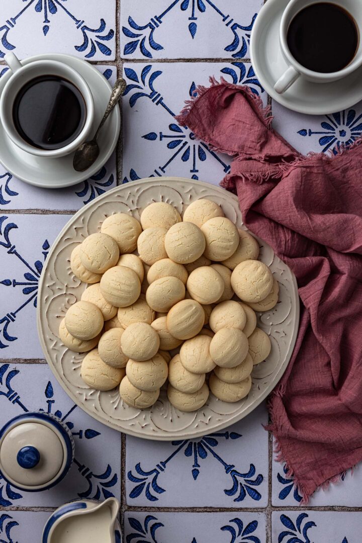 A platter of sequilhos (cornstarch cookies), two cups of coffee, a napkin , a sugar dish and a cream dish.