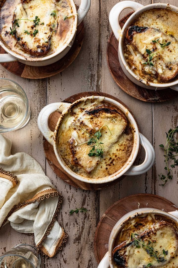 An overhead photo of three bowls of French Onion Soup. You can also see a napkin, two wine glasses and some thyme sprigs.