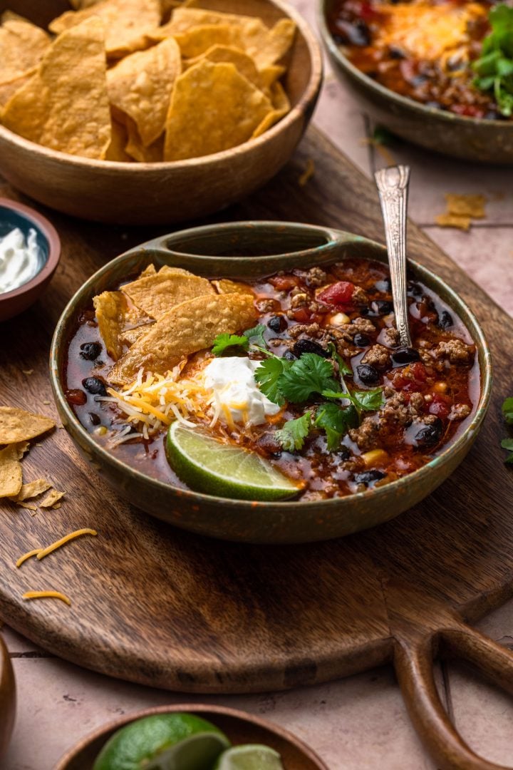 A bowl of taco soup, garnished with sour cream, cilantro, a lime wedge and tortilla chips.
