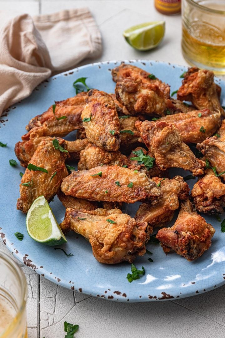 A platter of air fryer chicken wings, served with lime wedges and beer.