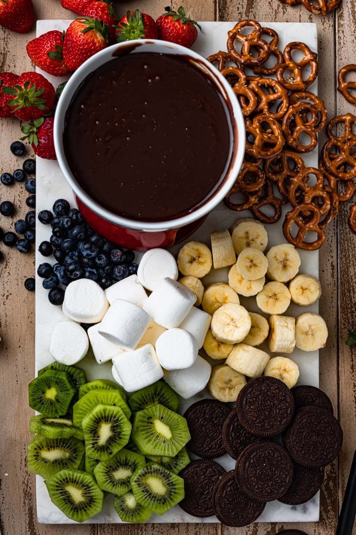 A pot of fondue on a board with several different dippers.