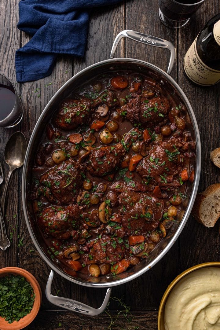 Coq au Vin in a serving dish, served with mashed potatoes and crusty bread on the side.