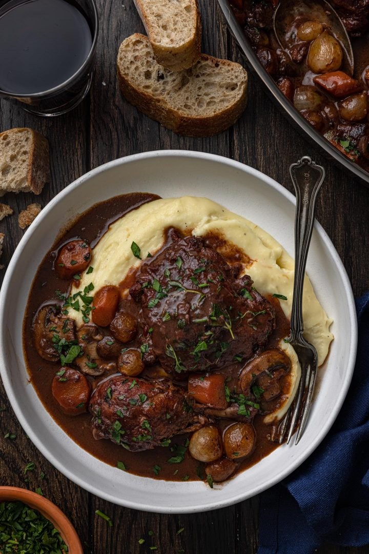 A close-up overhead photo of a bowl of chicken coq au vin over mashed potatoes.