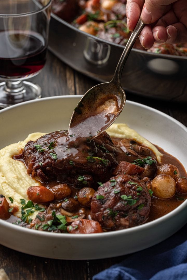 A spoon pouring the wine sauce over the chicken coq au vin.