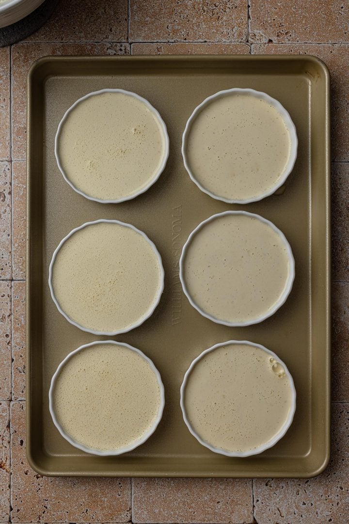 Custard in ramekins, on a baking sheet, ready to go in the oven.