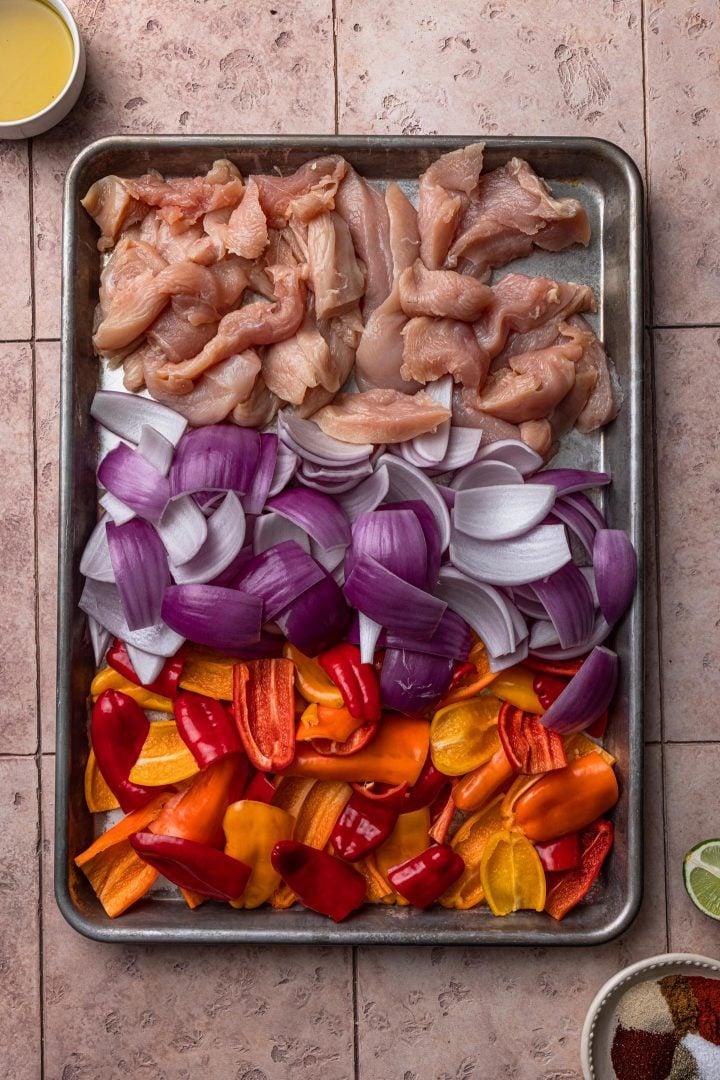 Chicken, onions and peppers in a baking sheet.
