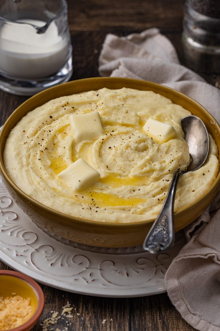 A bowl of cheesy mashed potatoes topped with butter.