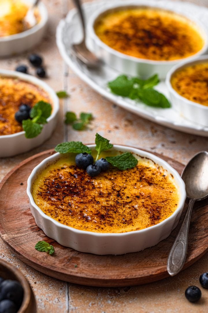 A close up photo of a creme brulee on a wooden plate, with a spoon.