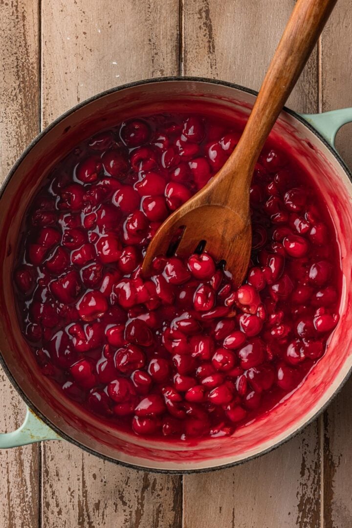 Homemade cherry pie filling in a pot with a wooden spoon.