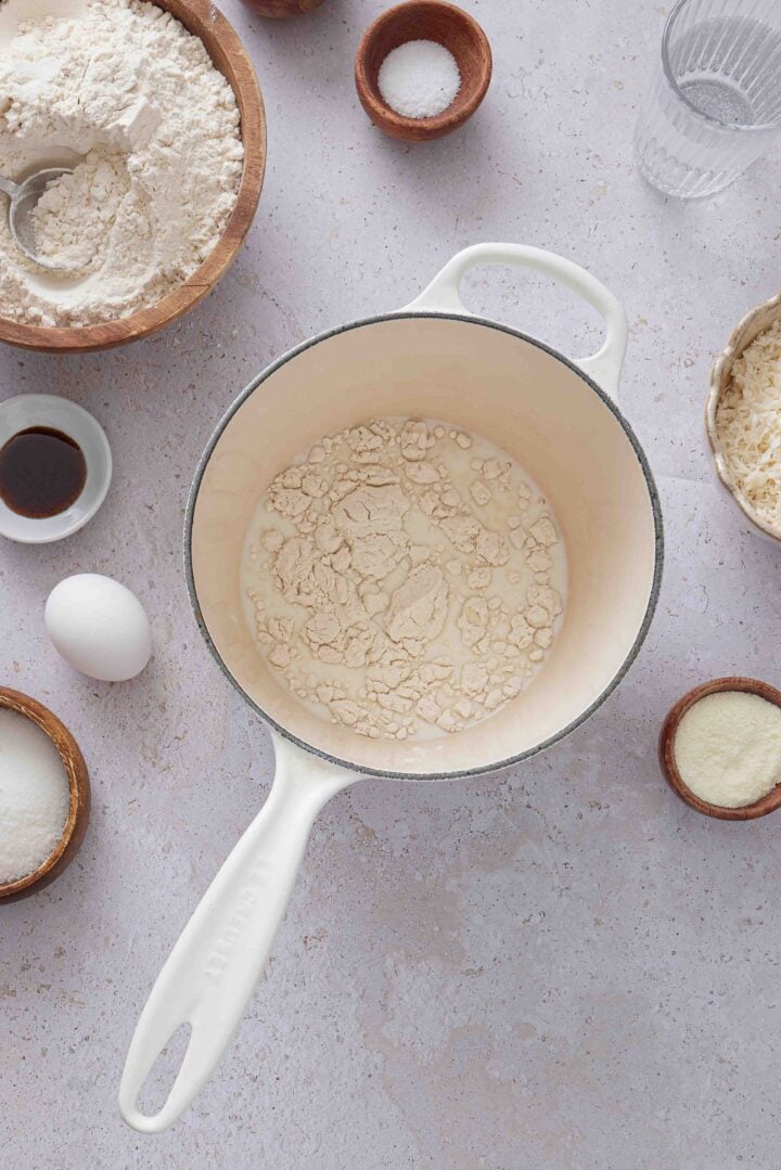 Overhead photo of flour and milk in a white saucepan, ready to make the tangzhong for Brazilian sweet condensed milk buns, with the other ingredients arranged around it.