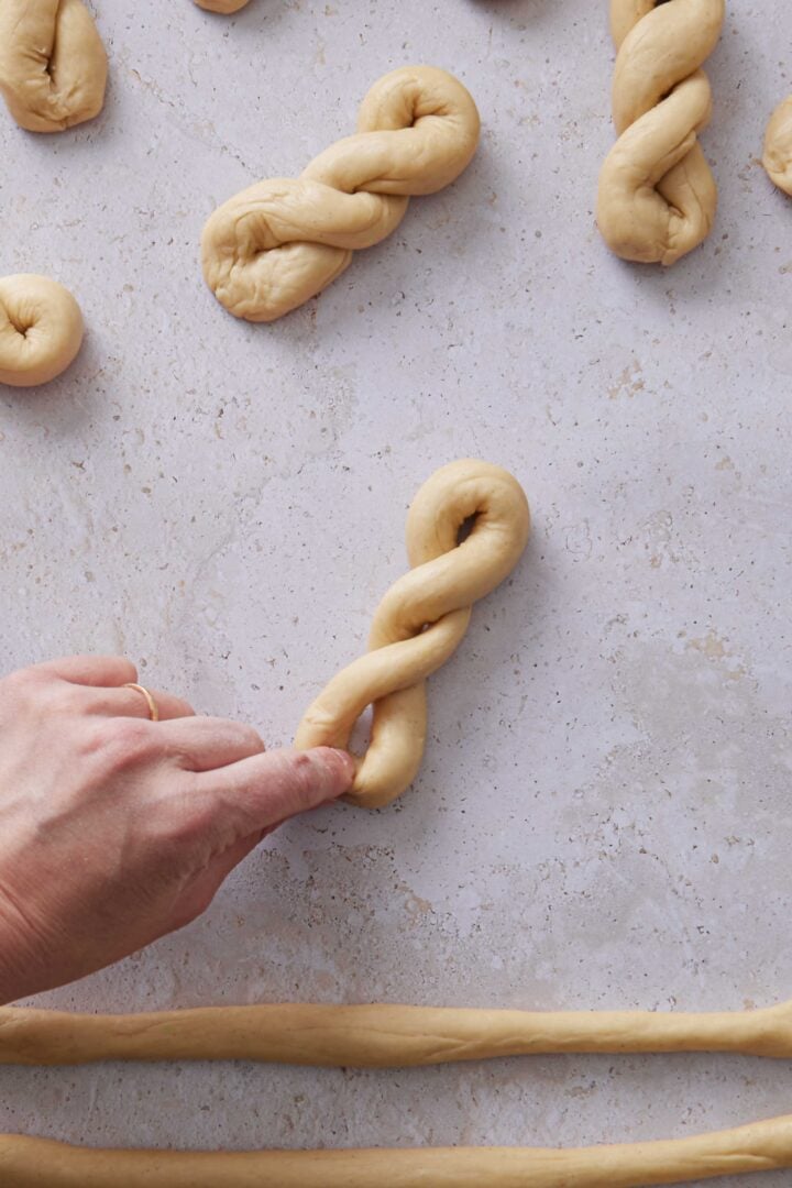 Overhead photo of a hand pinching the ends of a twisted dough bun to seal the shape.