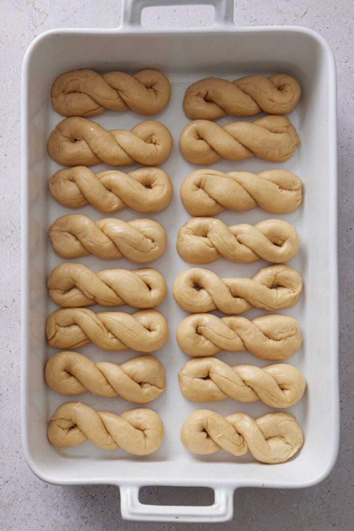 Overhead photo of shaped buns arranged in a white baking dish before the second rise.