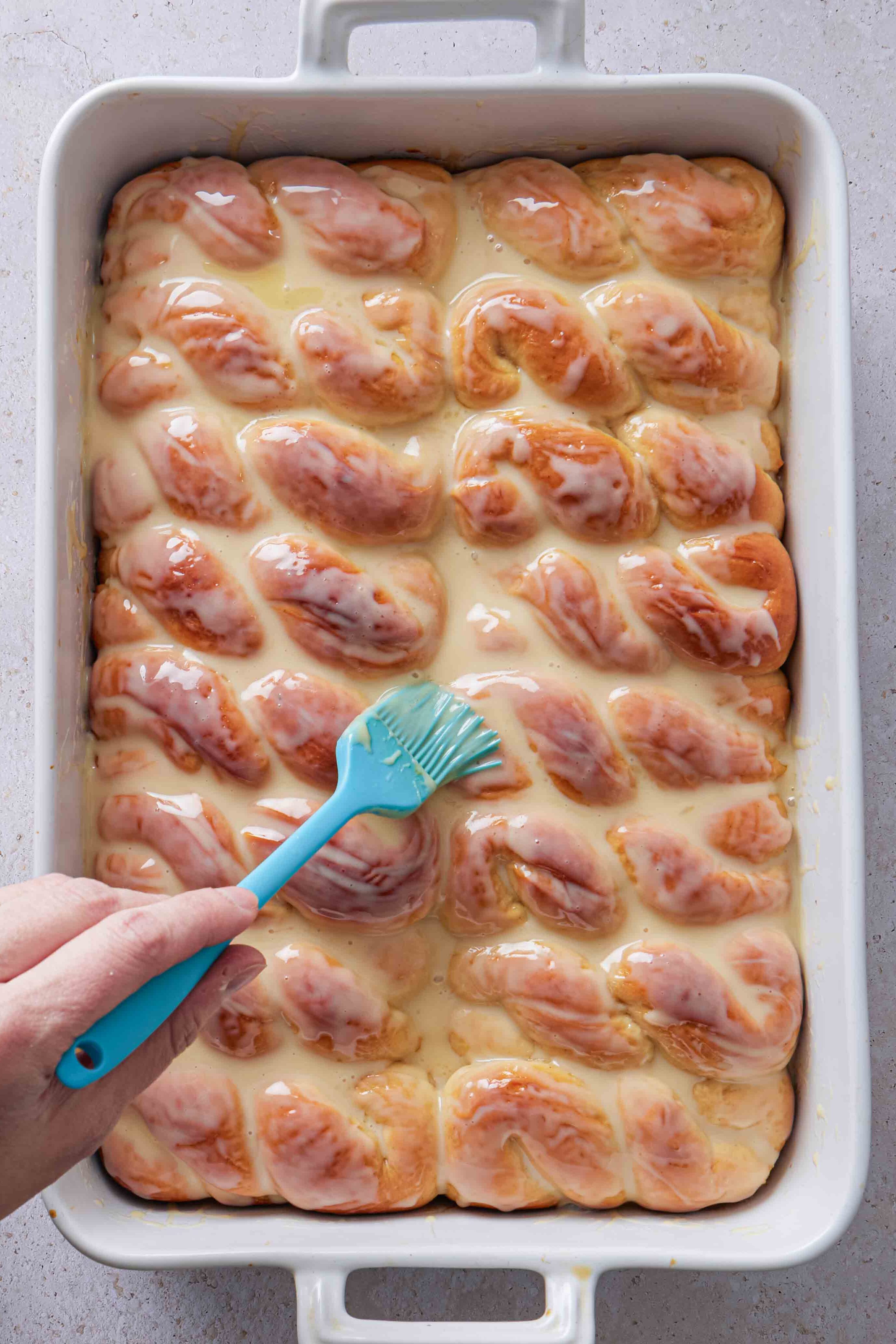 Overhead photo of sweetened condensed milk being brushed over the warm baked buns.