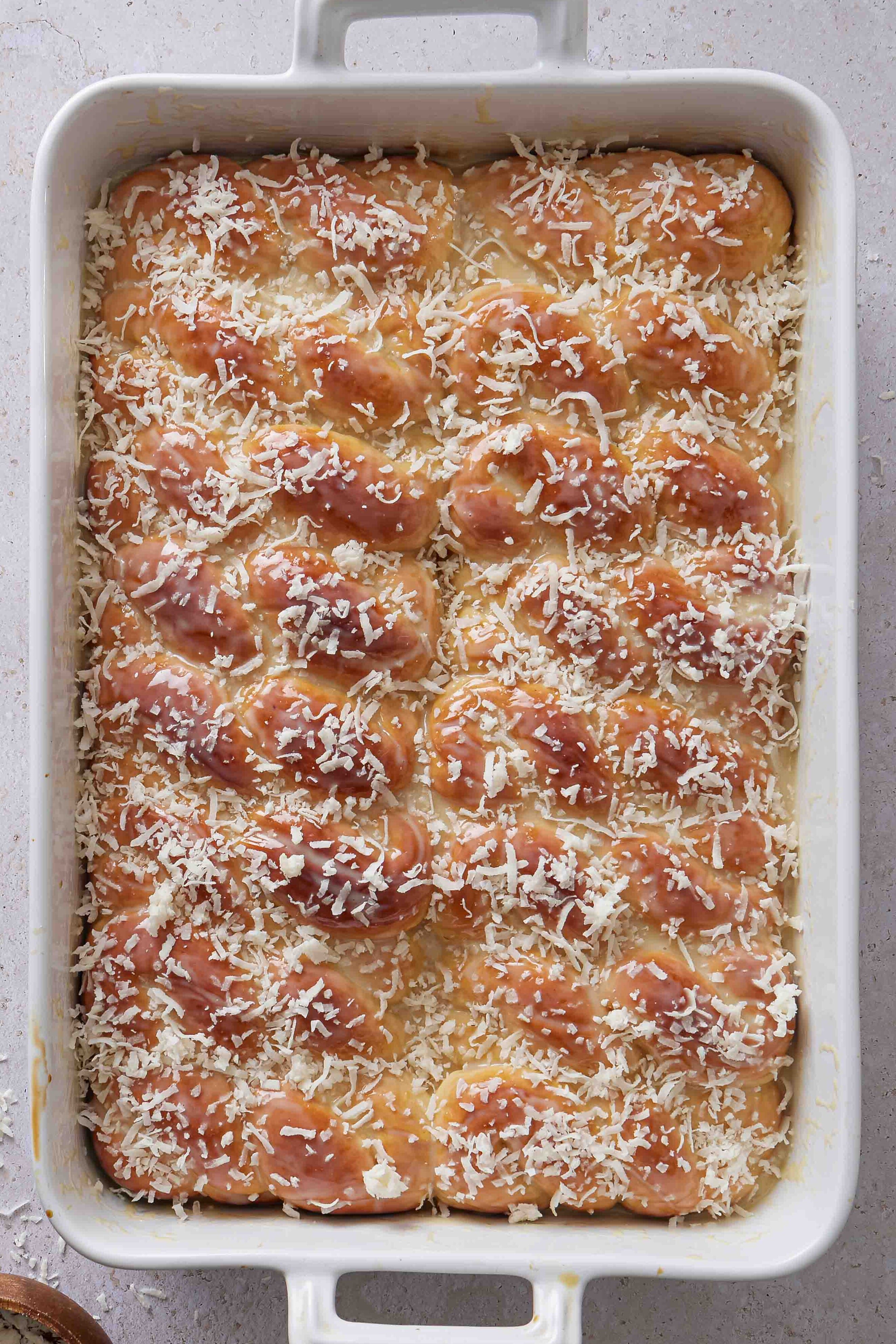 Overhead photo of sweetened condensed milk being brushed over the warm baked buns.