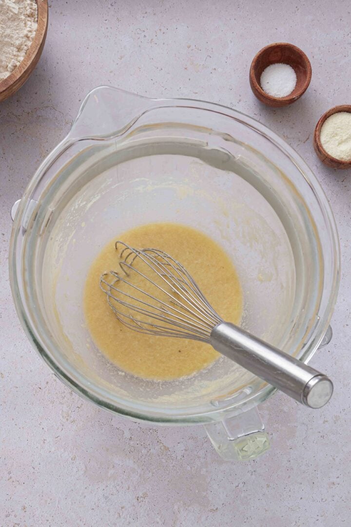 Overhead photo of the wet ingredients for Brazilian sweet condensed milk buns whisked together in a glass mixing bowl.
