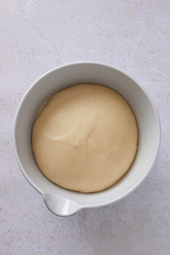 Overhead photo of risen dough in a white bowl after the first rise for Brazilian sweet condensed milk buns.