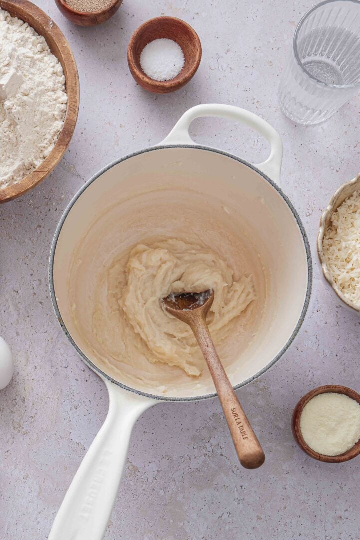 Overhead photo of the cooked tangzhong paste in a white saucepan with a wooden spoon, surrounded by ingredients for Brazilian sweet condensed milk buns.
