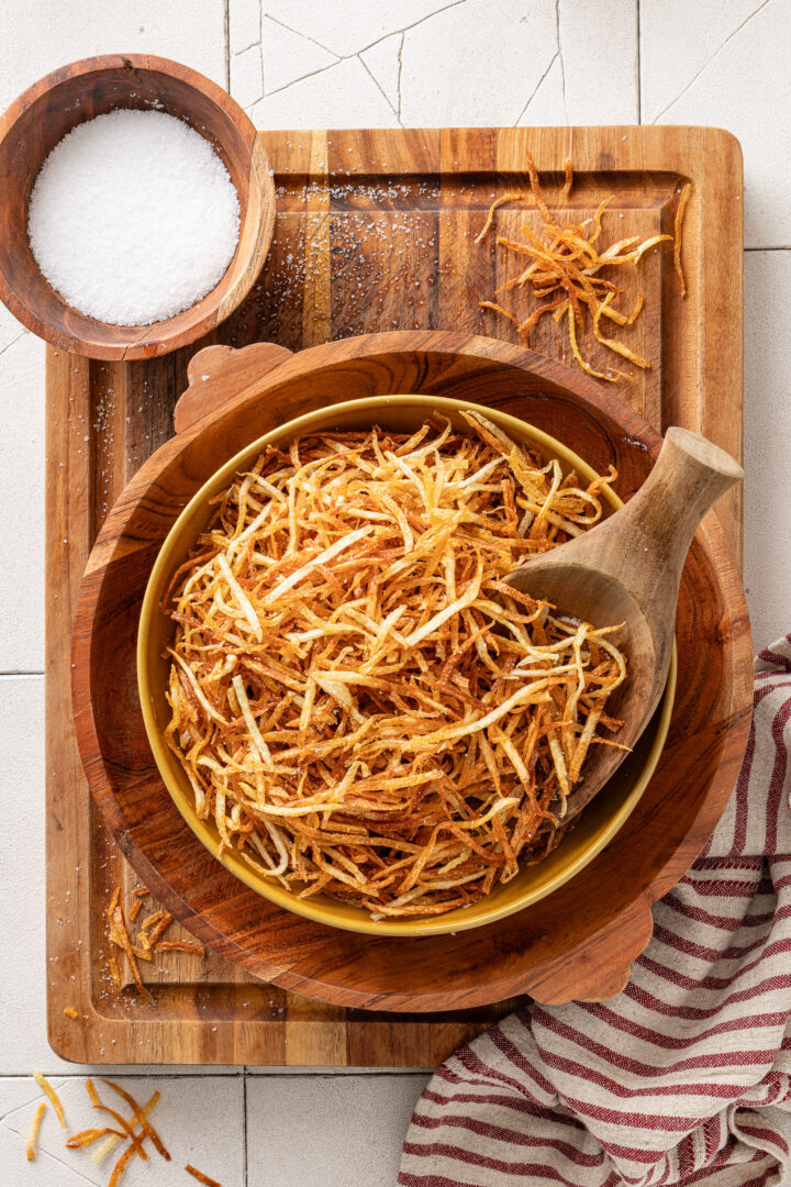 Bowl of homemade batata palha with crispy golden shoestring potatoes on a wooden surface.