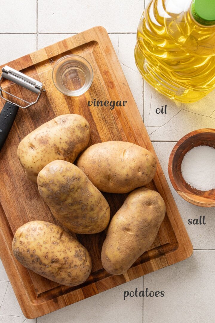 Ingredients for homemade batata palha including russet potatoes, oil, salt, vinegar, and a julienne peeler.