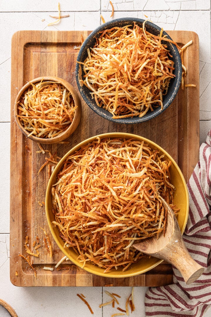 Several bowls filled with homemade batata palha showing a generous batch of crispy Brazilian shoestring potatoes.