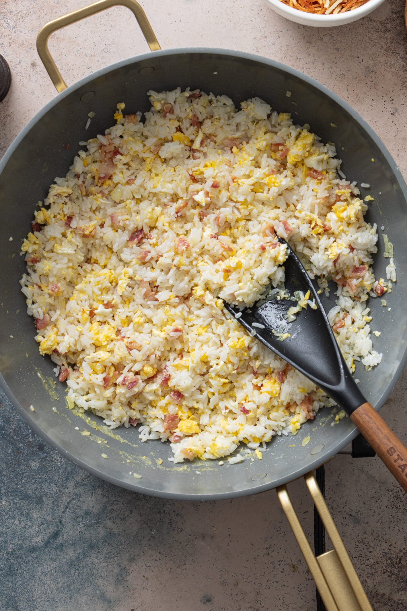 Cooked white rice added to skillet with bacon and eggs for arroz biro biro
