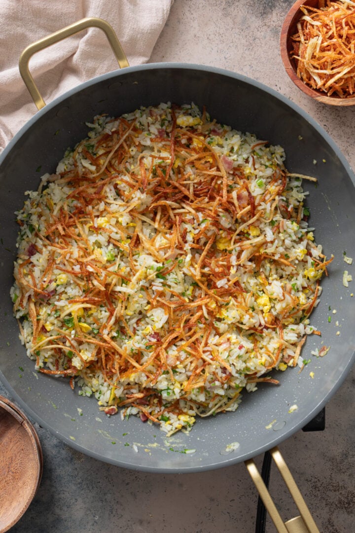 Arroz biro biro in skillet topped with crispy batata palha and herbs
