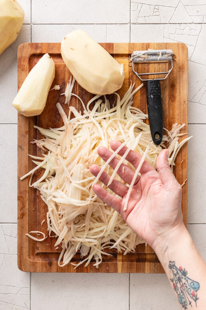 Hand holding thin julienned potatoes cut for homemade batata palha.