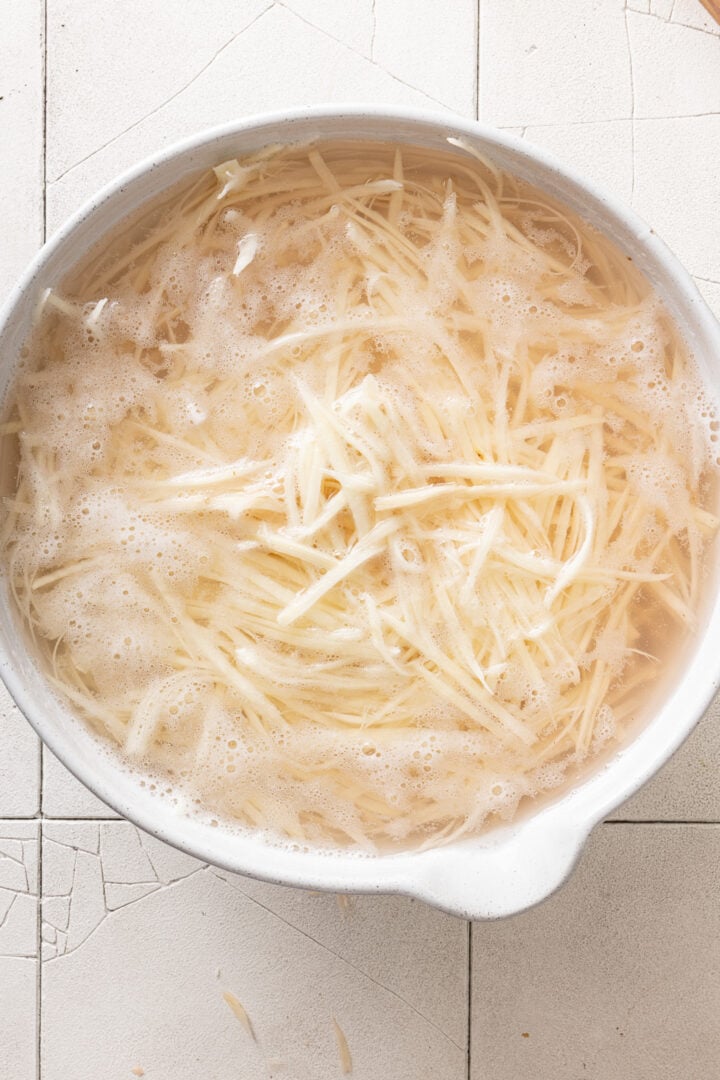 Julienned potatoes soaking in water to remove excess starch before frying.