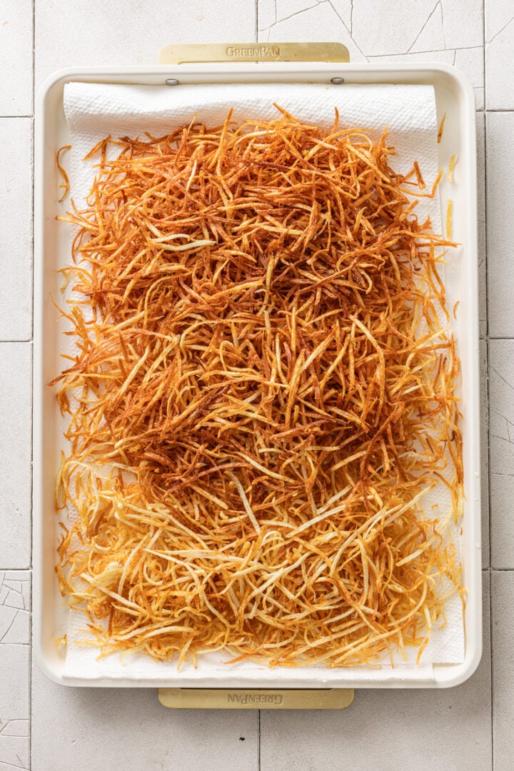 Freshly fried batata palha draining on a paper towel-lined tray.
