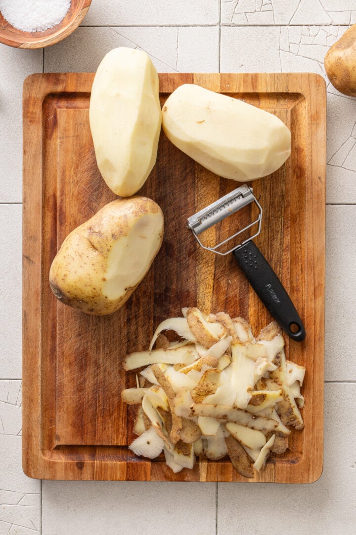 Peeled russet potatoes and julienne peeler for making homemade batata palha.