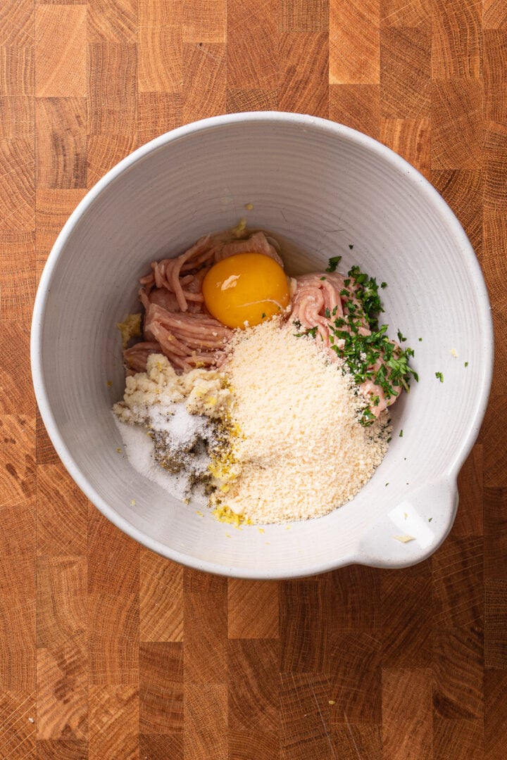 Ground chicken, egg, Parmesan, soaked bread, lemon zest, and parsley in a bowl for chicken piccata meatballs