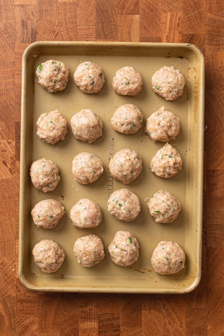 Raw chicken meatballs shaped and arranged on a baking sheet before cooking