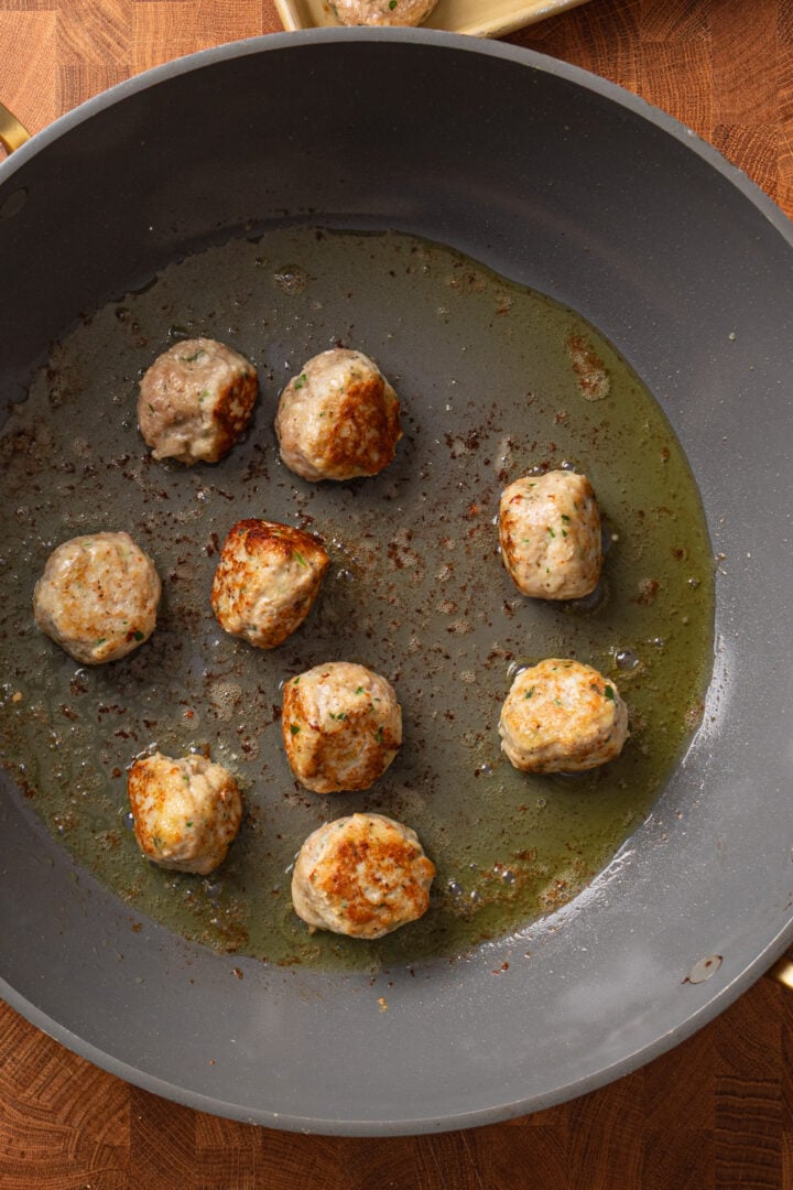Chicken meatballs browning in a skillet with olive oil until golden on the outside