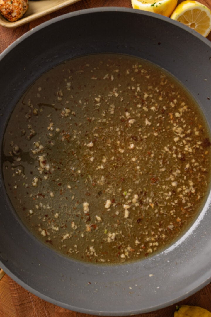 Garlic cooking in the skillet with browned bits to build flavor for piccata sauce, then deglazing with wine.