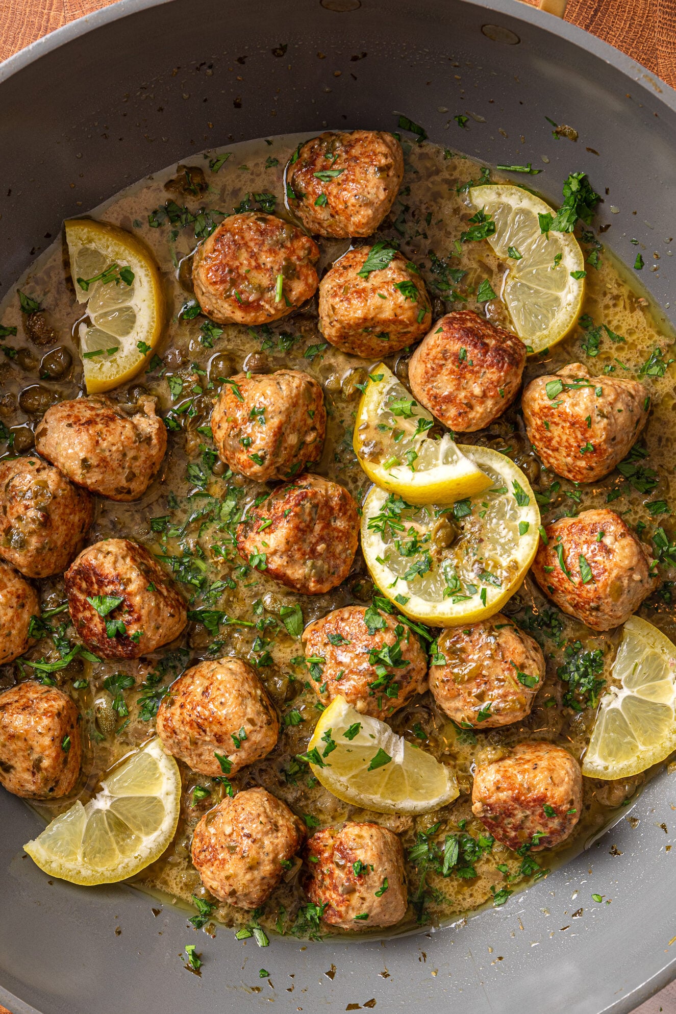 Chicken piccata meatballs in skillet with lemon slices, capers, and parsley in a light sauce
