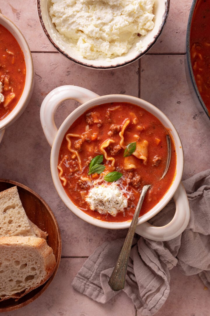 Overhead view of lasagna soup with ricotta, bread, and basil on a table