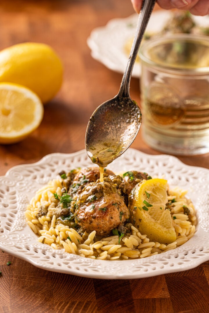 Spoon pouring lemon caper sauce over chicken piccata meatballs served with orzo pasta