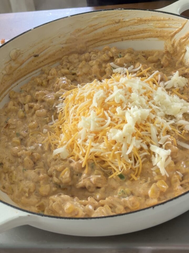 Shredded cheese and cotija added to creamy corn mixture for elote dip