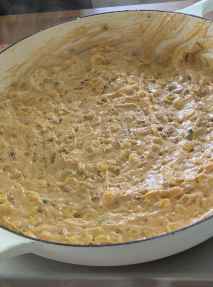 Warm creamy Mexican street corn dip mixture cooking in a skillet with melted cheese and corn