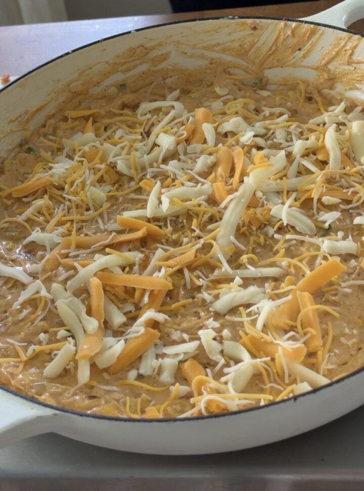 Mexican street corn dip in a skillet topped with shredded cheese before baking