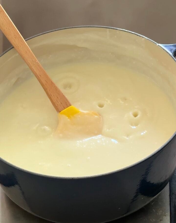 Thick coconut pudding mixture cooking in a pot, stirred with a spatula until smooth and creamy.
