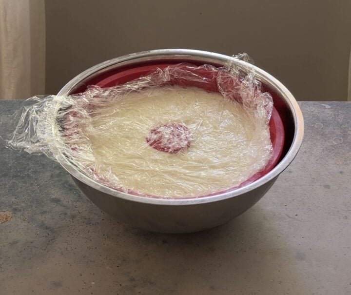 Brazilian coconut pudding poured into a bundt mold, covered with plastic wrap, and chilling to set.