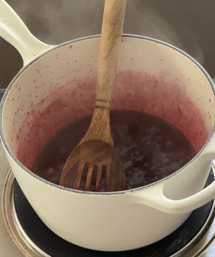 Homemade berry sauce simmering in a pot until thick and glossy.