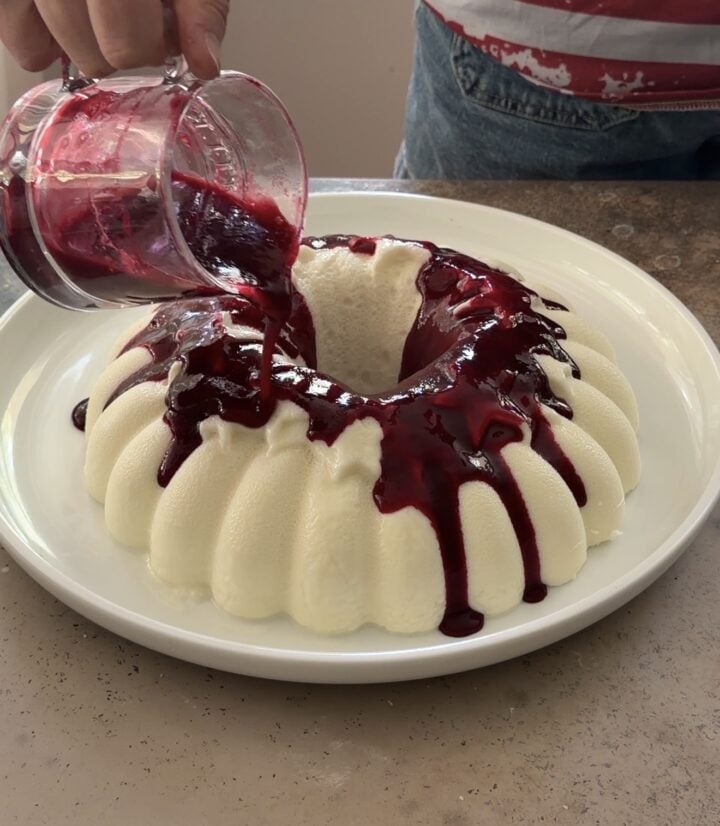 Berry sauce being poured over Brazilian coconut pudding on a white serving platter.