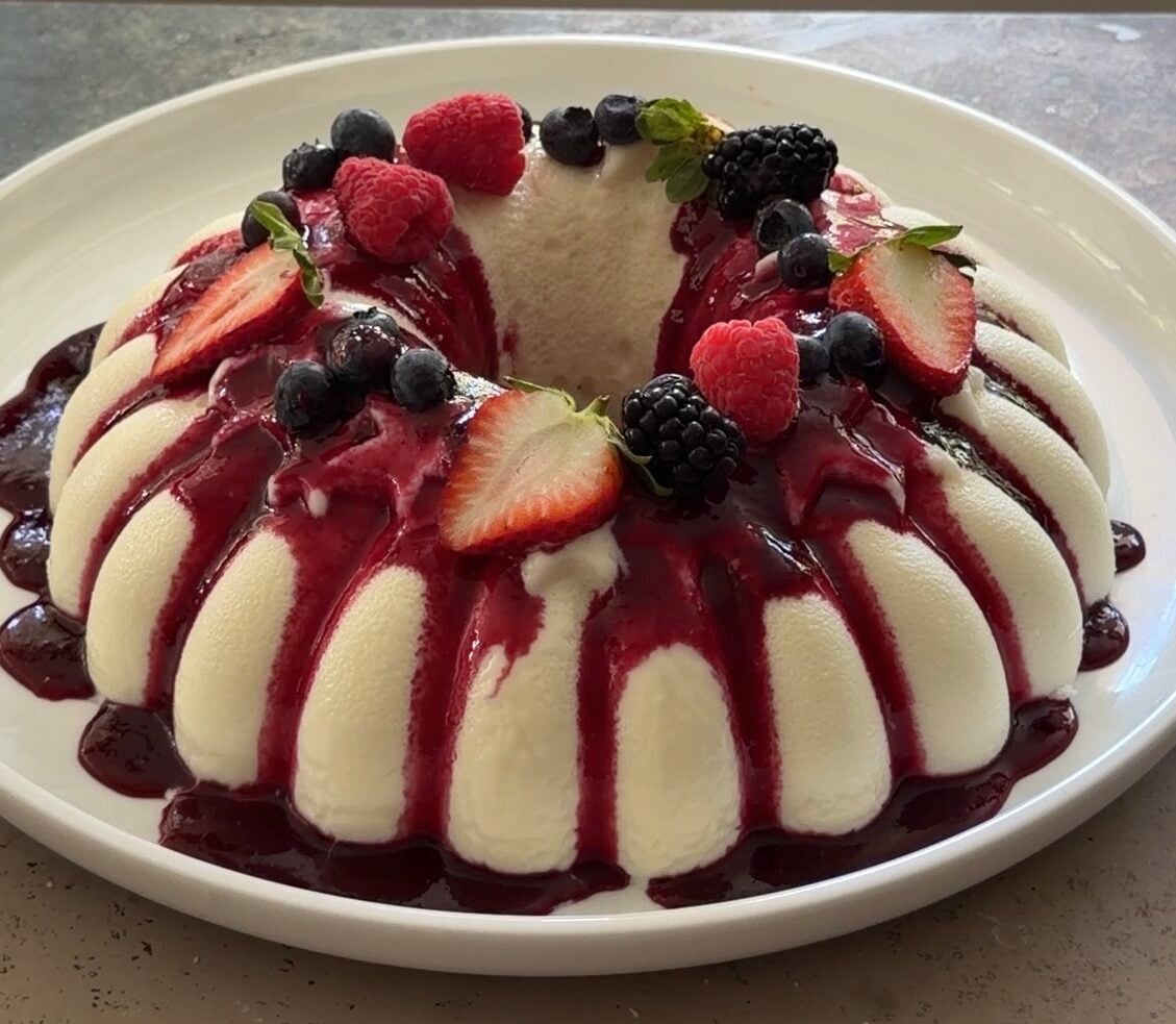 Brazilian coconut flan topped with berry sauce and fresh berrieson a white platter.