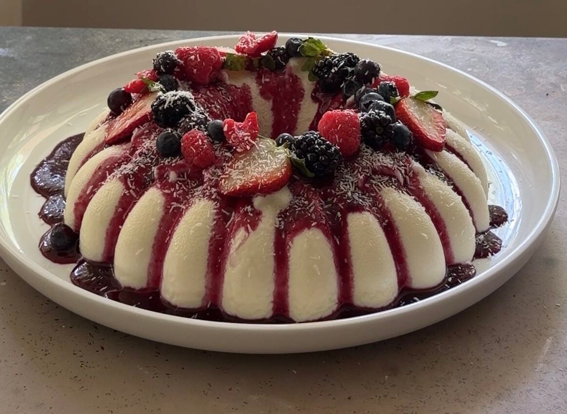 Brazilian coconut pudding with berry sauce, fresh berries, and shredded coconut, ready to serve.