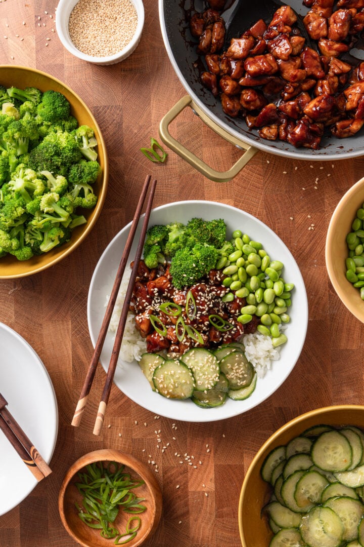 Overhead view of chicken teriyaki rice bowls with rice, broccoli, cucumber salad, and edamame